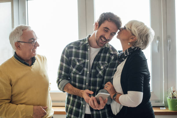 Young man looking at phone, his mother kissing him and father looking at them